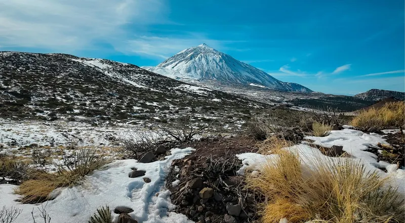 Snow lying on volcanic ground below a snow-capped Mount Teide